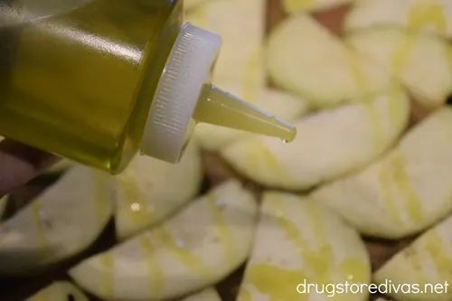 A squirt bottle of olive oil being squirted over sliced eggplant round halves on a sheet pan.