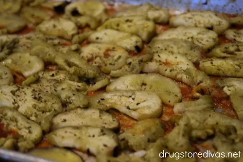 Eggplant round halves spread across a thin layer of marinara sauce at the bottom of a sheet pan.