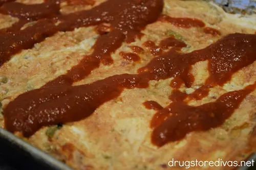 Marinara sauce in a drizzle on top of a cheese and sauce mixture in a sheet pan.