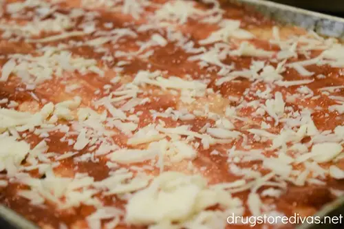 Shredded mozzarella cheese an sauce in a sheet pan.
