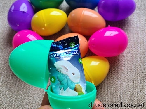 A teal plastic Easter egg with a chocolate bunny inside with other plastic Easter eggs behind it.