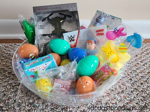 A clear bowl filled with white, iridescent paper shred and Easter treats. 