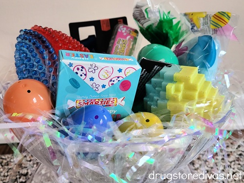 A clear bowl filled with white, iridescent paper shred and Easter treats.