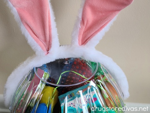 A headband with bunny ears on top of a clear bowl that's filled with Easter treats.