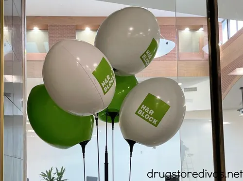 White and green balloons advertising H&R Block tax services in a doorway of a storefront.