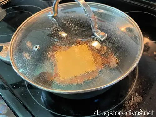 Cooked potato and ham hash with a slice of cheese on top in a pan with a lid on top.