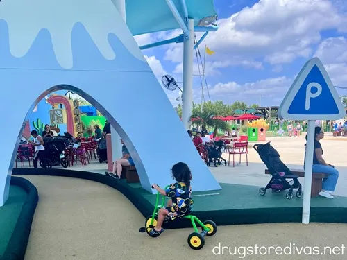 A boy with long hair riding a tricycle under a fake mountain in Peppa Pig Theme Park in Winter Haven, Florida.