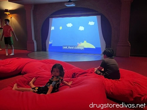 Two boys on red bean bag chairs in front of a large screen with a cartoon on it in Peppa Pig Theme Park in Winter Haven, Florida.