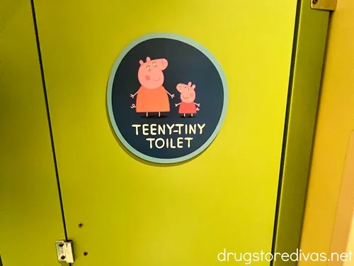 A round, blue sticker with two cartoon pigs on it that says TEENY-TINY TOILET on a green door.