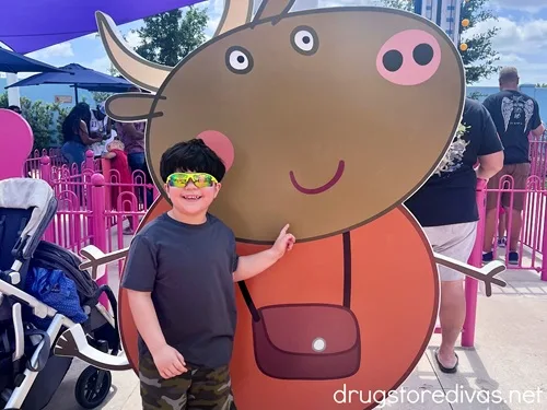 A boy standing in front of a cut out of a cartoon pig with a purse at Peppa Pig Theme Park in Winter Haven, Florida.
