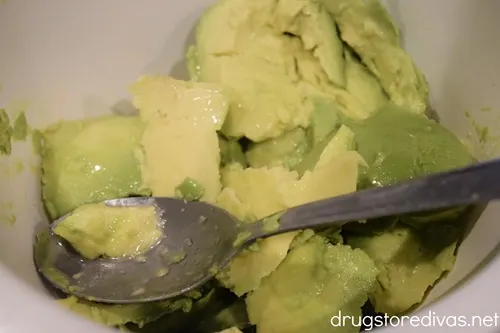 Piece of avocado and a silver spoon in a white bowl.
