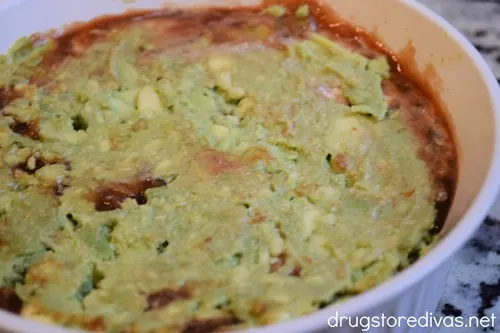 Mashed avocado on top of salsa in a white, round casserole pan.