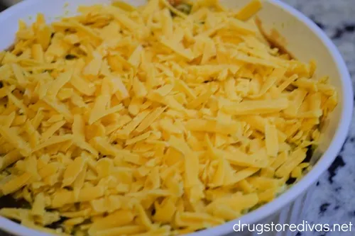 Shredded cheddar cheese on top of salsa in a white, round casserole pan.