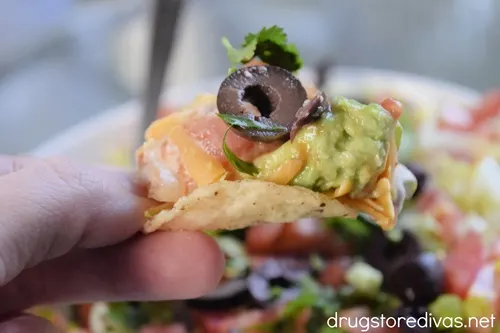 Two fingers holding a tortilla chip scoop that's filled with taco dip.