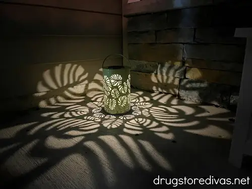 A solar lantern that's projecting light in the shape of monstera leaves on the ground of a front porch.