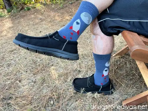 A man's legs showing him wearing black loafers and a pair of blue socks with a rocket ship on them.