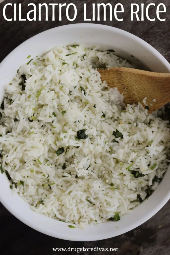 A white, round bowl filled with rice with cilantro in it with a bamboo spoon to the right inside of the bowl with the words "Cilantro Lime Rice" digitally written on top.