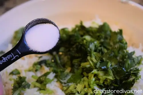 A measuring spoon filled with salt over a bowl of chopped cilantro and cooked rice.