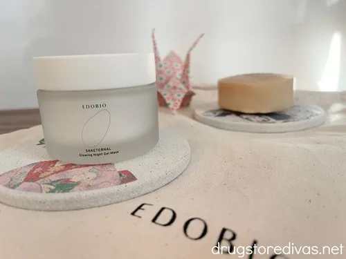A small night cream and round bar of soap from Edobio on Japanese-themed soap holders with an origami crane behind them.