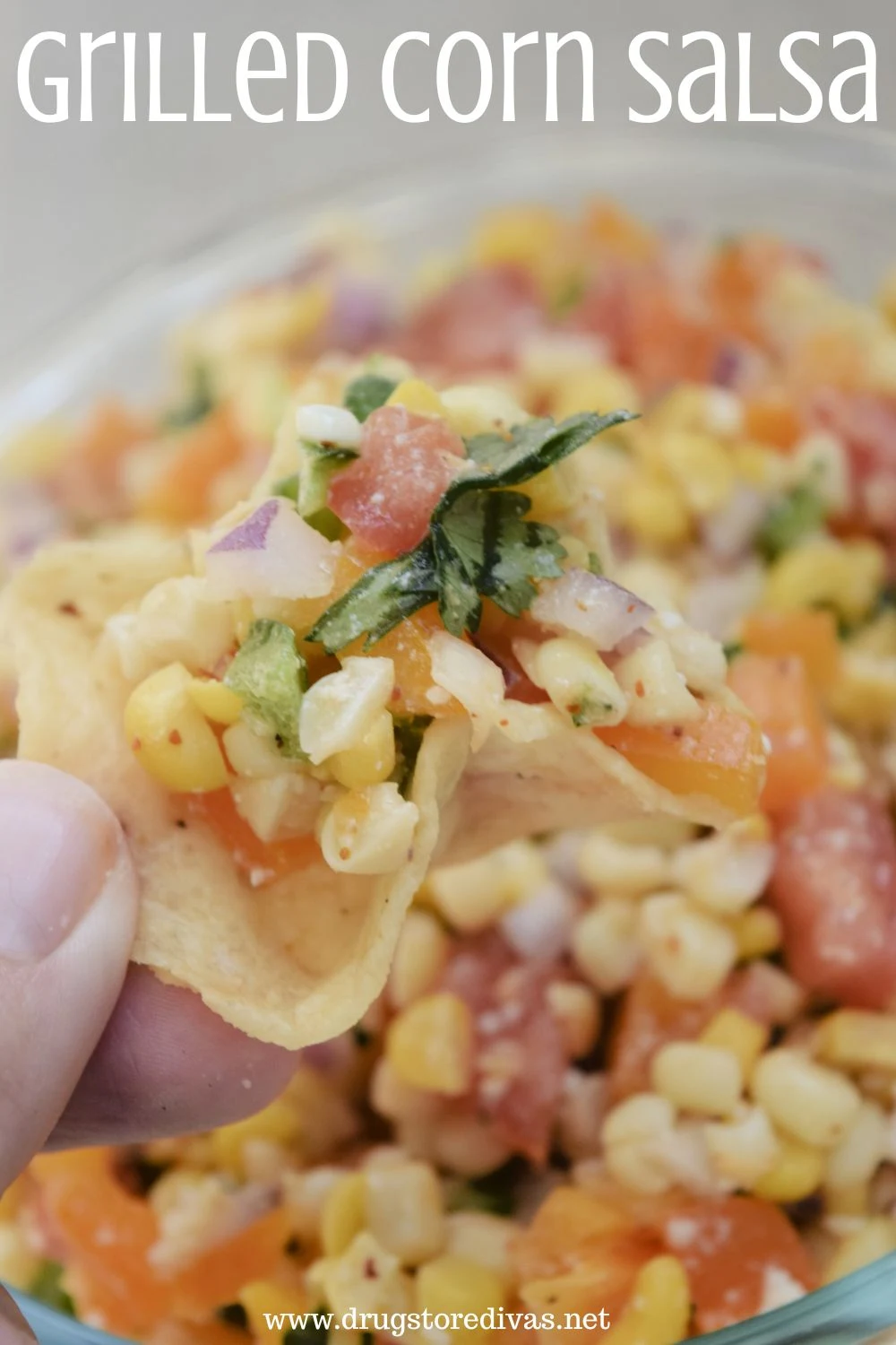 A hand holding a tortilla chip that has corn salsa in it over a bowl of the salsa with the words 