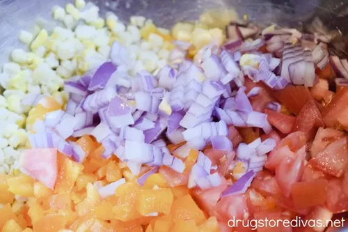 Diced orange bell pepper, Roma tomatoes, red onion, and corn kernels in a bowl.