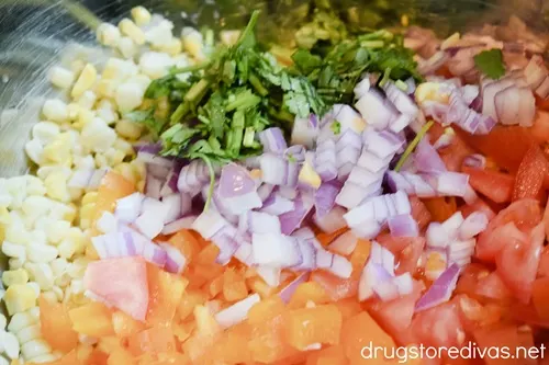 Diced orange bell pepper, Roma tomatoes, red onion, corn kernels, and fresh cilantro in a bowl.