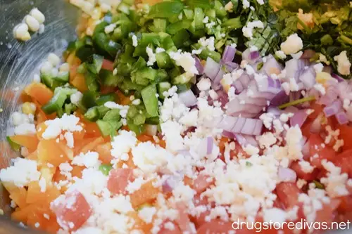 Diced orange bell pepper, Roma tomatoes, red onion, corn kernels, jalapeno peppers, fresh cilantro, and crumbled queso fresco in a bowl.