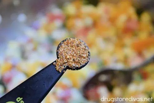 A measuring spoon with seasoning in it over a bowl of vegetables.