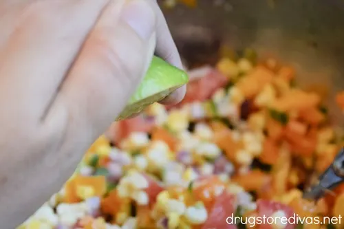 A hand squeezing half a lime into a bowl of corn salsa.