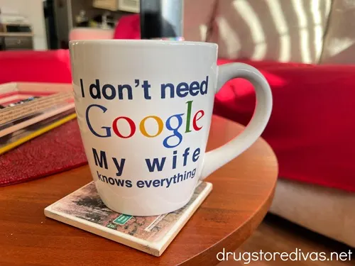 A mug that says "I don't need Google my wife knows everything" on a coaster on a table in a living room.