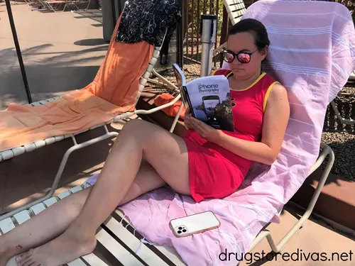 A woman in a dress reading a book on a pool lounge chair.