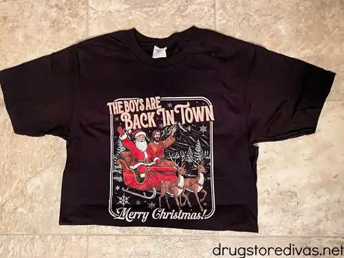 A black t-shirt with an image of Santa and Jesus in a sleigh with the words "The Boys Are Back In Town" above the image and "Merry Christmas" below the image.
