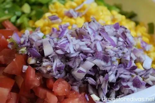 Chopped tomato, corn, green pepper, and diced red onion in a white bowl.