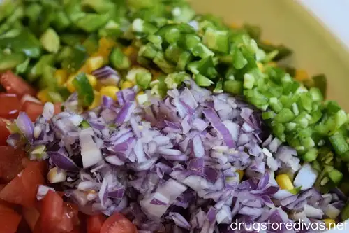 Chopped tomato, corn, green pepper, and diced red onion in a white bowl.