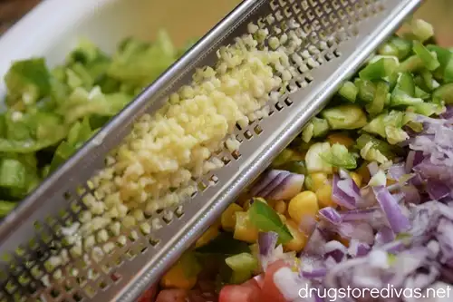A zester filled with garlic over a bowl of vegetables.