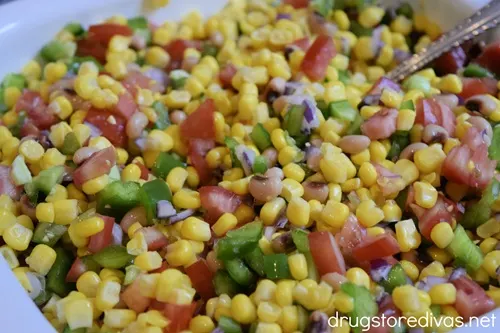 Corn, diced red onion, green pepper, tomatoes, and black eyed peas in a white bowl.