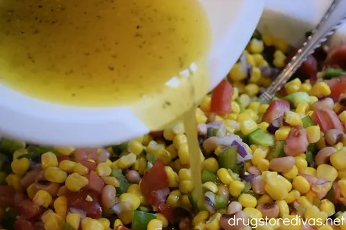 Olive oil with seasoning in a white bowl being poured onto diced vegetables.