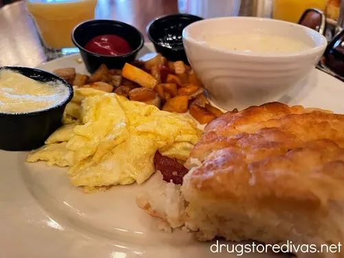 A breakfast plate with scrambled eggs, a biscuit, grits, home fries, jelly, ketchup, and butter, served at Clark's Inn in Santee, SC.