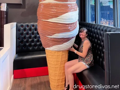 A woman sitting on a black cushioned wrap around bench holding onto a giant ice cream cone.