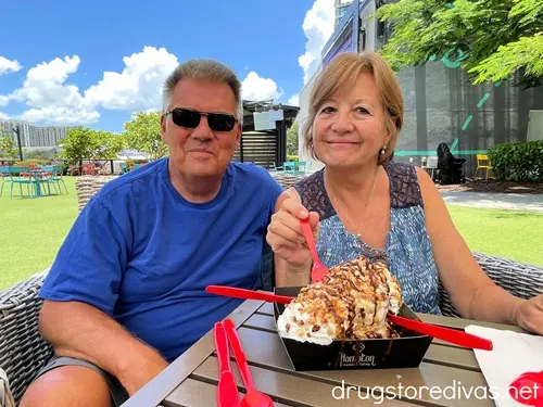 A man in a blue t-shirt and sunglasses and a woman in a blue tank top with a large plate on ice cream on a table in front of them.