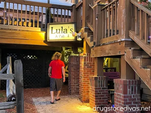 A man with long hair, wearing a red shirt and black shorts, walking into an underground bar called Lula's A Pub in Wilmington, NC.
