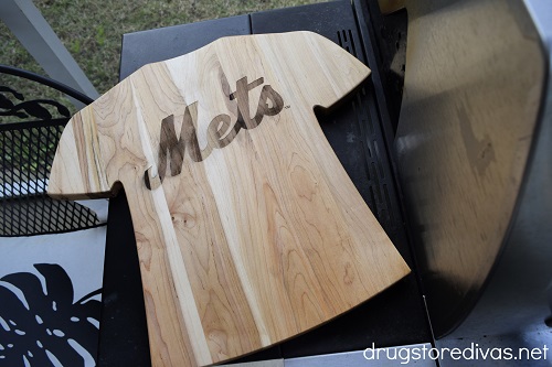 A cutting board shaped like a shirt with the New York Mets name on it on the side of a grill.
