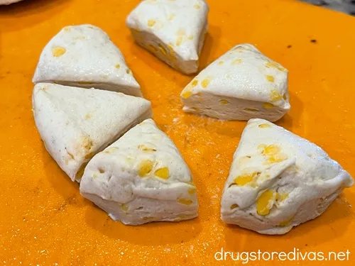 A round, raw biscuit cut into six pieces on an orange cutting board.