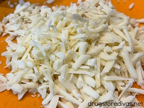 Shredded mozzarella cheese on an orange cutting board.
