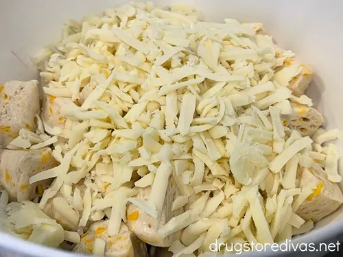 Shredded mozzarella cheese on top of biscuit dough pieces in a white bowl.