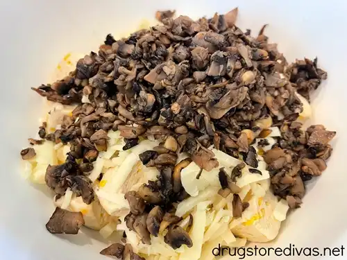 Cooked mushroom pieces and shredded mozzarella cheese on top of biscuit dough pieces in a white bowl.