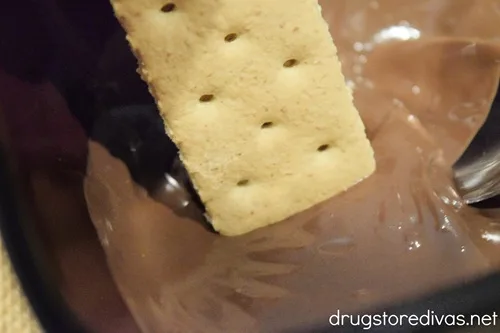 A graham cracker being dipped into melted chocolate.