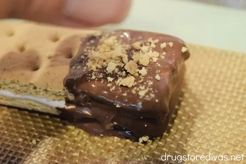 Fingers above a graham cracker that has been dipped in chocolate crumbling graham cracker on top of the chocolate.