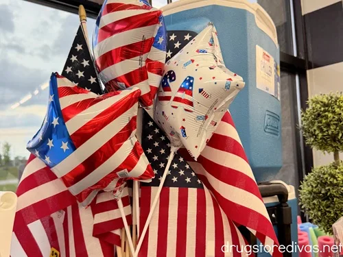 Star shaped balloons with an American flag design on then, another that says USA, and American flags available for sale in a store.