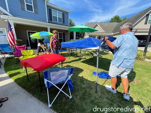 Three men and a woman setting up pop up tents in a front lawn of a house.